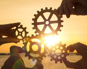 four people businessman holding gears on a sunset background. concept of teamwork. coherence, strategy, cooperation, group.
