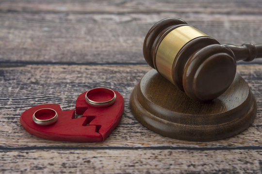 Wedding rings on the figure of a broken red heart, gavel, hammer of a judge on a wooden background. Divorce proceedings, the dissolution of marriage, the division of property.