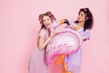 Two girls with hair curlers and flamingo baloon. They are celebrating women's day March 8.