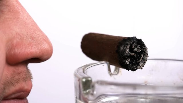 a man sniffs a cigar that lies in an ashtray, close-up