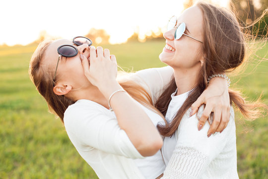 Two nice women are enjoying life on the green field at sunset.