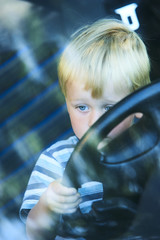Little child boy sitting in front of the car holding steering wheel