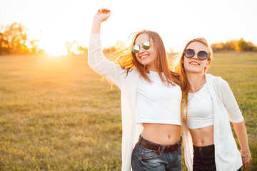 Two beautiful females are walking on a field at sunset. Best friends