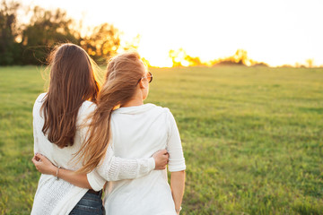 Two young women are looking forward tothe sunset on the green field.