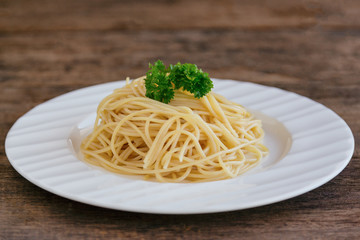Boiled spaghetti with al dente level. Cooked pasta prepared for cooking on white plate decorated with fresh parsley in side view, copy space on wood table. Homemade Italian traditional food concept.