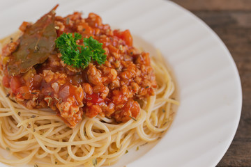 Spaghetti bolognese sauce with beef or pork,cheese,tomatoes and spices on white plate on wood table, top view with close up. Homemade delicious Italian traditional food for lunch or dinner.