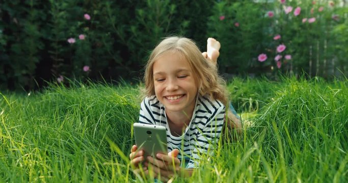 Laughing girl lying on grass with cell phone. Dolly shot