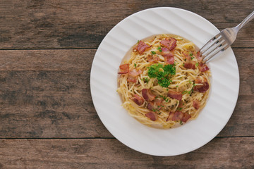 Spaghetti carbonara with bacon, cheese and chopped parsley on wood table in top view flat lay with copy space. Italian traditional homemade food for lunch or dinner so creamy and delicious.