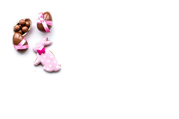 Sweets for Easter table. Chocolate eggs near cookies in shape of Easter bunny on white background top view copy space