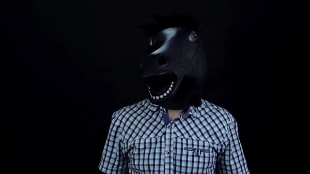 Man in a horse mask nods his head dancing isolated on a black background slow motion