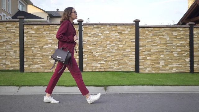 Side view of a businesswoman wearing glasses and a red suit texting on her way to work on a summer day. Suburbs Tracking real time medium shot