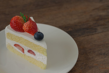 Strawberry shortcake on white plate put on wood table with copy space. Delicious and soft vanilla sponge cake with dairy whipped cream and fresh strawberries and blueberry. Homemade bakery concept.