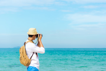Fototapeta na wymiar Summer Day. Happy smiling caucasian tourist asian young man holding camera for take a photo check in on the beach. Summer and Travel Concept.