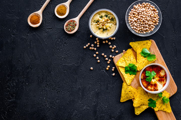 Hummus ready to eat. Bowl with dish among pieces of crispbread and spices on black background top view copy space