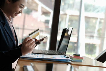 woman holding a credit card and using smart phone for online shopping at cafe. businesswoman purchase goods from internet at office. female adult make payment on bank website at workplace