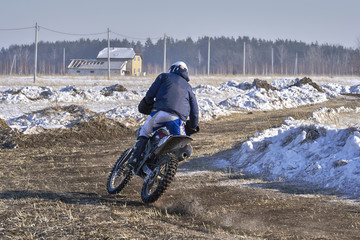 Sportsman racer man fulfills a fast ride on a motorcycle on the road extreme. The race track is very uneven. Sunny frosty winter day.