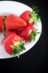 Fresh strawberries on plate on black background