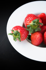 Fresh strawberries on plate on black background