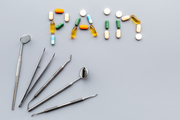Toothache, dental pain. Fear of dental treatment. Word pain lined with pills near dentist tools. Grey background top view copy space