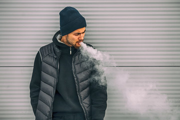 Vape man. Portrait of a handsome young white guy in black waistcoat and modern cap vaping an...