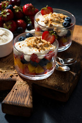 Assorted fresh fruit with custard in glasses on a dark background, vertical