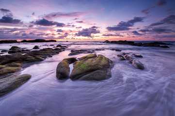 Long expose seascape with rocks covered by green moss and waves trails. soft focus due to slow shutter.