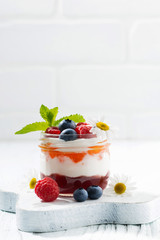 dessert with jam, cream and fresh fruit in a glass jar, vertical
