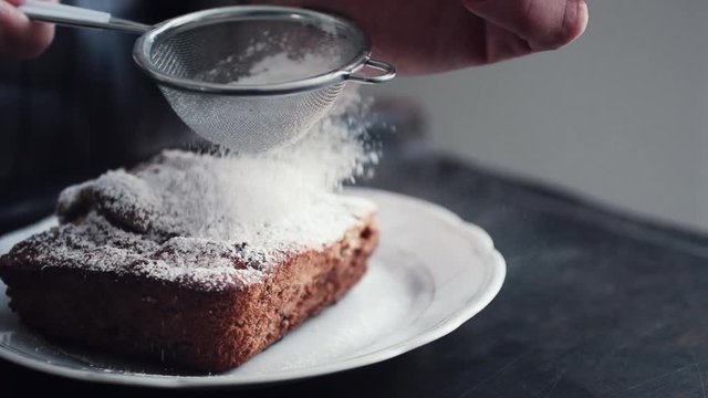 Slow motion shot hands of cook adding powdered sugar on the peice pie as a topping