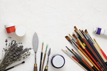 Fototapeta premium Professional brushes for artists, palette knives, colorful paints and dried lavender branches lie on a white canvas