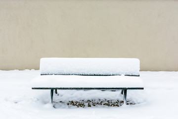 Front view of a public wooden bench covered in snow in front of a wall in the Trocadero garden in Paris.