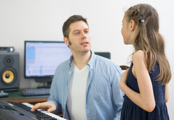 Male vocal coach teaching little girl how to sing. Focused on girl.