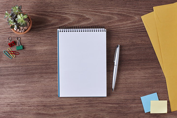 Office Workspace. Top View of a Business Workplace. Wooden Desk Table, Pen, Pencil, a Blank Notebook, Envelope, Plant Pot, Clips. Copy space for text or Image