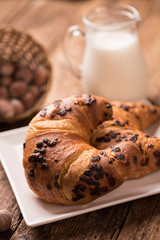 Fresh croissant on a wooden board  with milk. Freshly baked croissant on a dark wooden table.