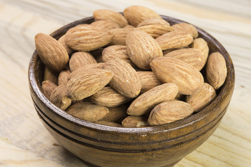 Almonds in brown bowl on textured wooden background, top view. Copy space on left side