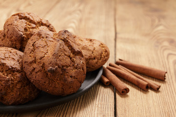 Handmade cookies from oats lie on a black tray and cinnamon sticks lie on an old wooden table