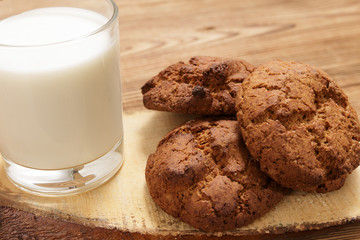 Three pieces of homemade oatmeal cookies and a glass of milk stand on a tray on a wooden brown one...
