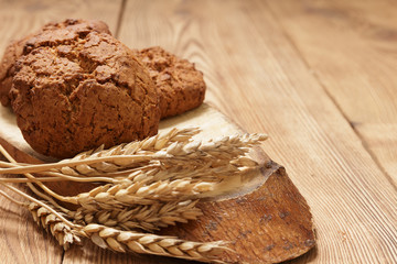Three pieces of homemade oatmeal cookies and wheat spikes lay on a piece of wood on the side of a brown old table