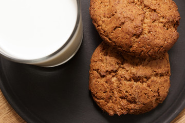 Two pieces of homemade oatmeal cookies and a glass of milk stand on a black wooden tray