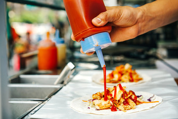 A close-up, a man's hand with a bottle of ketchup running food on the street. Street Shawarma.