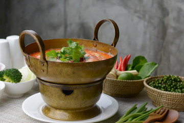 Creamy Tom Yum Goong (Thai spicy shrimp soup) in hot pot on the table and gray cement background.