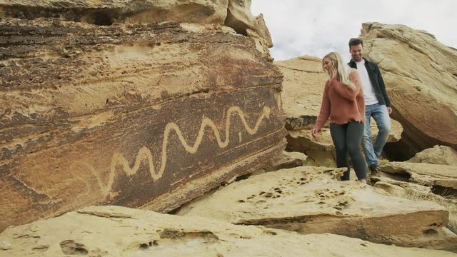 Couple hiking on rocks stopping to admire ancient artwork / Moore, Utah, United States