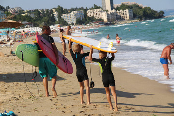 Two boys on the seashore help the father with carrying of surfboards.