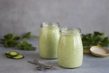Green organic smoothies in glass jars on a gray background.