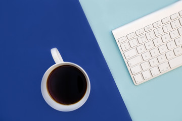 Coffee cup and computer keyboard on minimal bright blue background