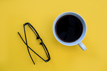 Minimal coffee cup and eyeglasses on bright yellow background