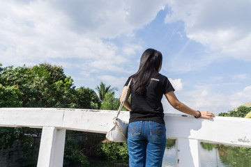 Fototapeta na wymiar Back view of young adult woman wearing black shirt standing on old bridge and look at the sky with copy space for text., nature concept. goal concept. decision concept.