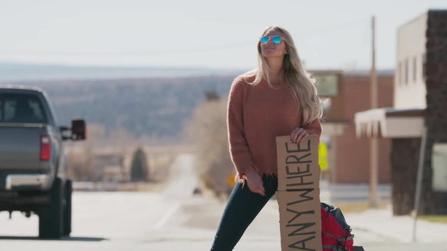 Woman holding anywhere sign hitchhiking on remote rural road / Loa, Utah, United States