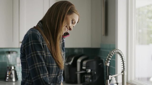 Woman washing pan talking on cell phone and dropping it into sink / Alpine, Utah, United States