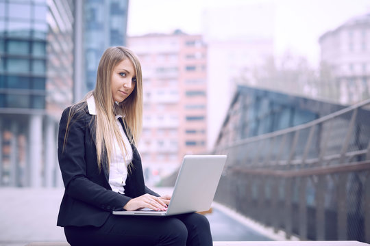 beautiful businesswoman using laptop and talking to mobile in urban environment