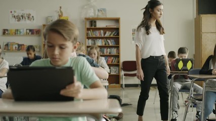 Panning shot of teacher assisting children in classroom reading digital tablets / Provo, Utah, United States - Powered by Adobe